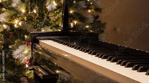 A hybrid player grand piano with modern technology features. Lit up Christmas tree in the background in bokeh. Inside the living room of an upscale American home. Piano made in Japan.