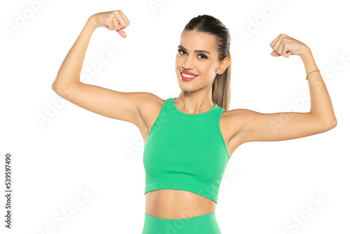 young sporty smiling woman in green shorts and top showing biceps on white background