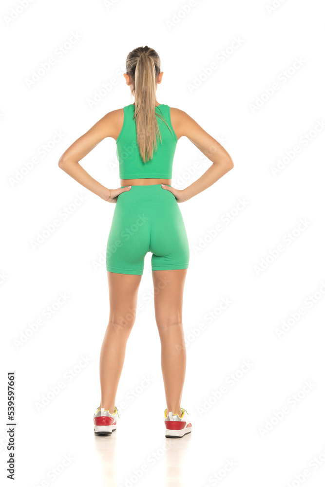 young sporty woman in green shorts and top posing on white studio background. Back view young sporty woman in green shorts and top posing on white studio background. Back view