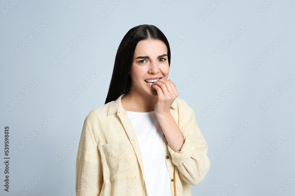 Young woman biting her nails on light grey background Young woman biting her nails on light grey background