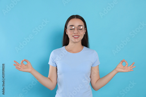 Find zen. Beautiful young woman meditating on light blue background