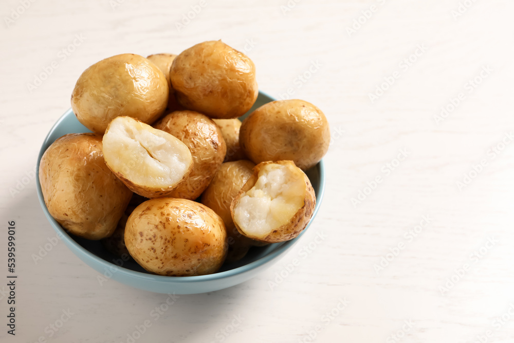 Bowl of tasty whole baked potatoes on white table, space for text Bowl of tasty whole baked potatoes on white table, space for text