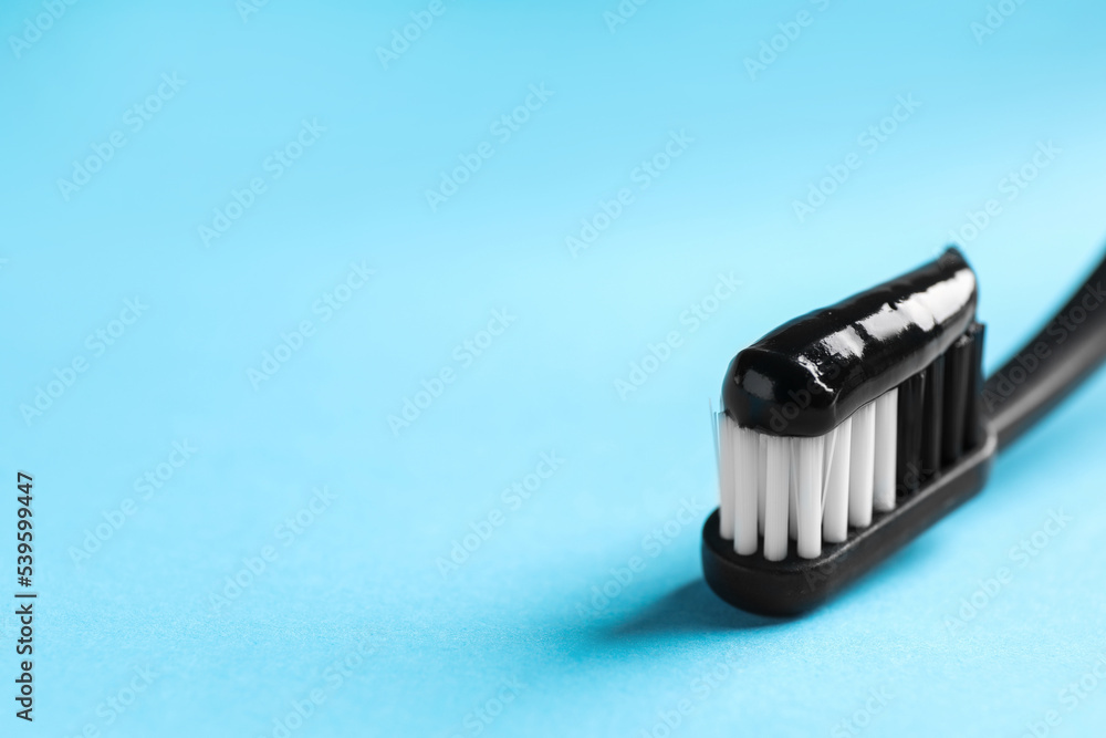 Brush with charcoal toothpaste on light blue background, closeup. Space for text Brush with charcoal toothpaste on light blue background, closeup. Space for text