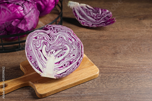 Whole and cut fresh red cabbage on wooden table, space for text