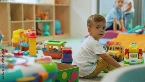 Small white boy playing with toy car in nursery during playtime surrounded by colorful toys and other kids. Multiracial group. Horizontal video . High quality 4k footage photo