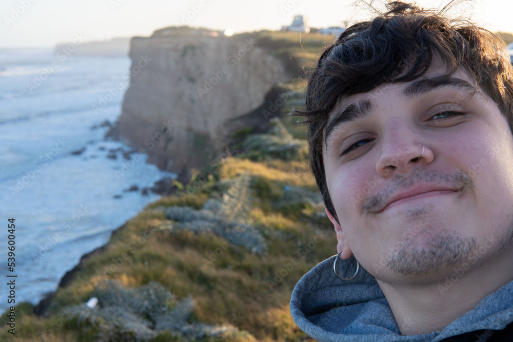 Naklejka premium self portrait of a young adult on top of a cliff at sunset. Happy guy smiling and looking at camera. Cliffs of Mar del Plata, Argentina