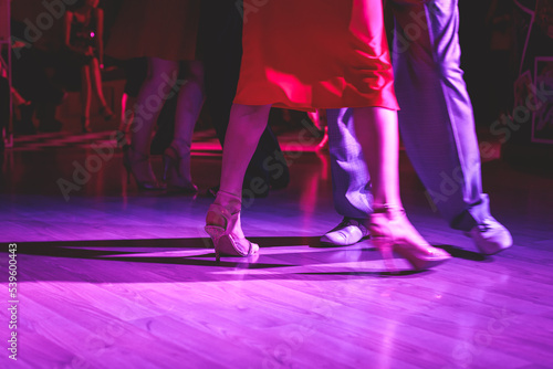 Dancing shoes of a couple, couples dancing traditional latin argentinian dance milonga in the ballroom, tango salsa bachata kizomba lesson, festival on a wooden floor, purple, red and violet lights photo