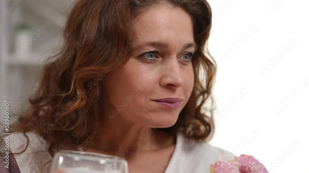 Close-up of happy brunette woman with grey eyes eating tasty doughnut drinking coffee smiling. Satisfied Caucasian mature lady enjoying morning snack at home indoors Close-up of happy brunette woman with grey eyes eating tasty doughnut drinking coffee smiling. Satisfied Caucasian mature lady enjoying morning snack at home indoors
