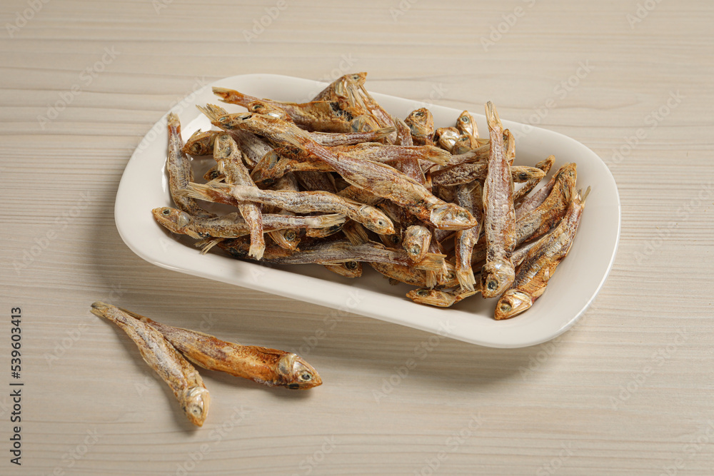 Plate of tasty dried anchovies on light wooden table Plate of tasty dried anchovies on light wooden table