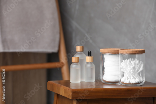 Cotton pads and swabs near cosmetic products on wooden stool in room. Space for text