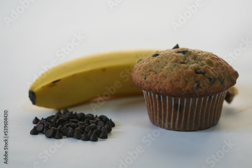 Banana chocolate chip muffin with banana and small pile of chocolate chips.