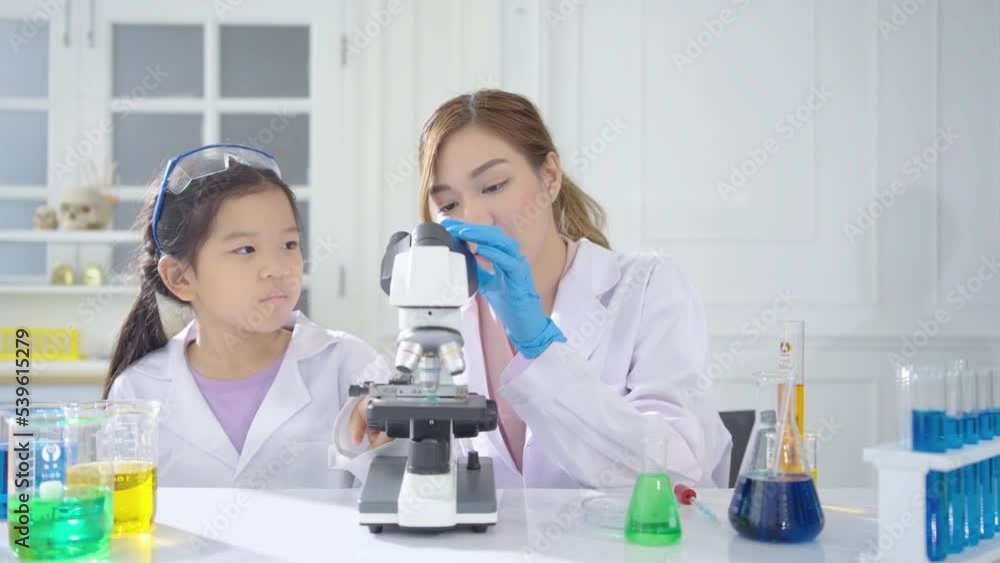 Asian woman teacher with child girl wearing coat are focusing on color mixing experiment in a test tube and focusing on a microscope in school science lab, Concept education, Science experiments Asian woman teacher with child girl wearing coat are focusing on color mixing experiment in a test tube and focusing on a microscope in school science lab, Concept education, Science experiments