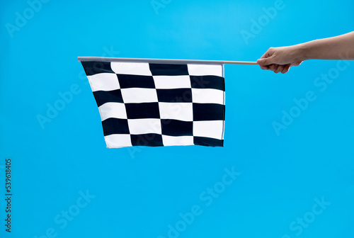 Human hand holding checkered flag on blue background
