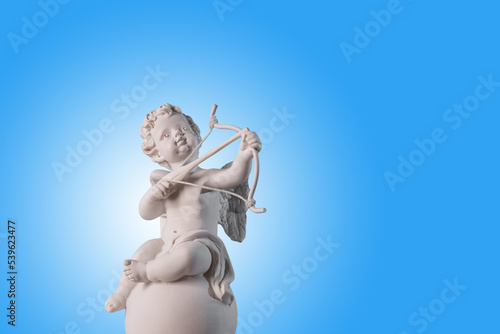 Figurine of an angel Cupid on the podium with a bow and arrow on a blu background . Valentine's Day.Place for text. photo
