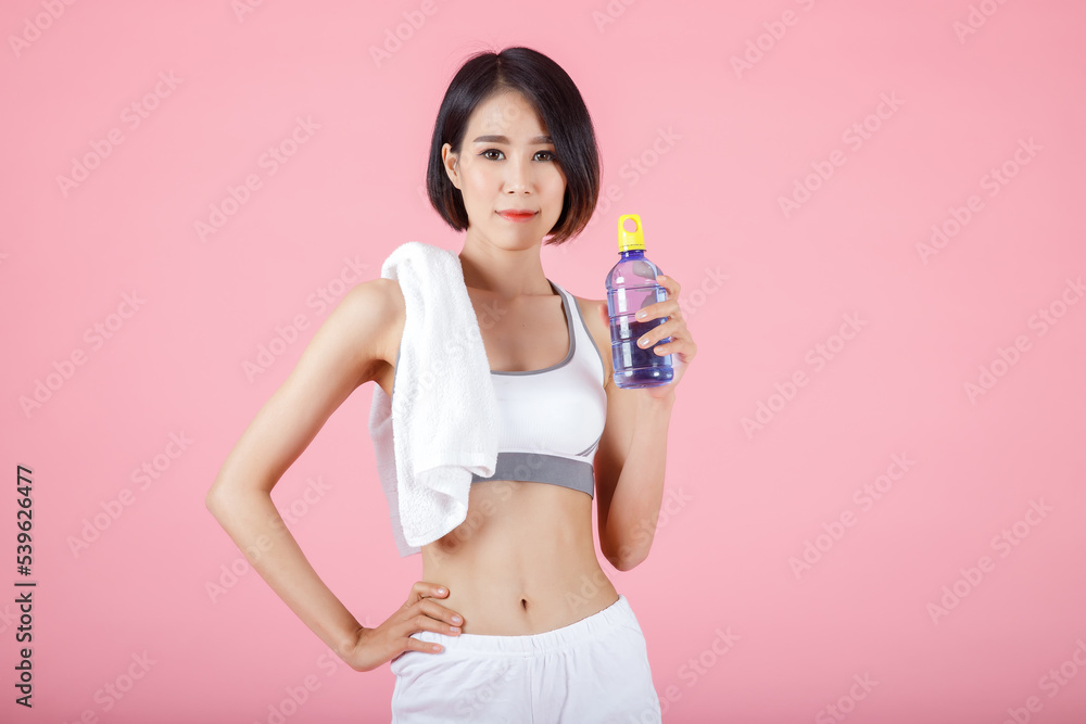 Portrait of smiling sporty woman with towel on her shoulder and holding drinking bottle of water on pastel pink background. Portrait of smiling sporty woman with towel on her shoulder and holding drinking bottle of water on pastel pink background.