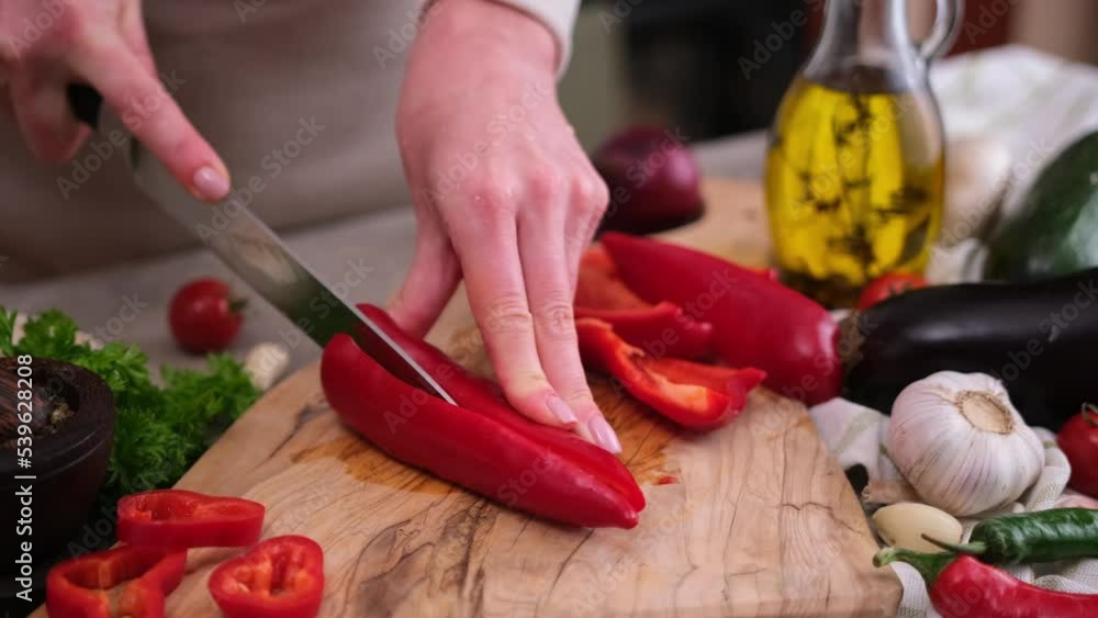 Woman cutting slicing fresh red pepper with a knife on a wooden board Woman cutting slicing fresh red pepper with a knife on a wooden board