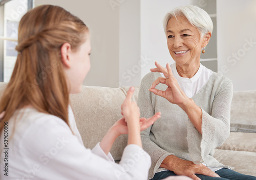 Senior woman, sign language and deaf girl communication, talking or conversation in home. Support, care and retired old female speaking to child with hearing disability in asl language hand gestures. photo
