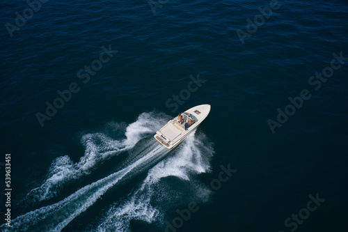 White boat with people on dark water top view. Speed open boat fast moving on dark water diagonally aerial view. © Berg