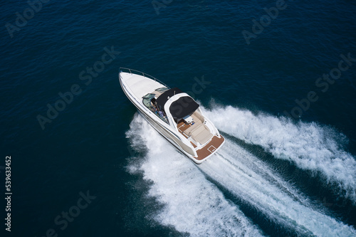 Speedboat fast moving on dark water diagonal aerial view. White boat with people on dark water top view. © Berg