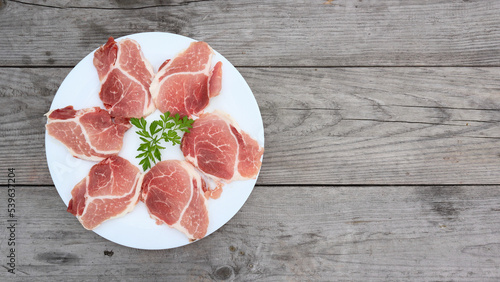 Raw Pork Slice in White Round Plate on old Wooden Table. Slide raw meat on the table decorated with parsley on a white plate