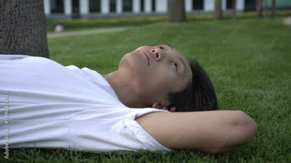 Thoughtful Asian man lies in the park on the grass. Sad or dreamy lonely teenager outdoors. Thoughtful Asian man lies in the park on the grass. Sad or dreamy lonely teenager outdoors.