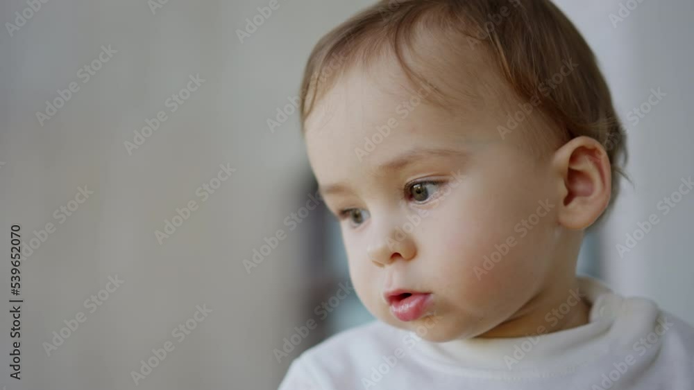 Nice calm Caucasian kid staring at one point. Beautiful toddler with adorable cheeks sitting peacefully indoors. Close up. Blurred backdrop. Nice calm Caucasian kid staring at one point. Beautiful toddler with adorable cheeks sitting peacefully indoors. Close up. Blurred backdrop.