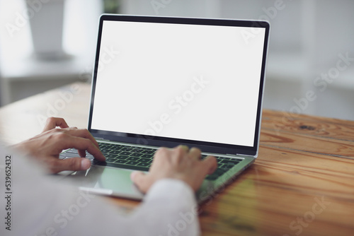 woman using and typing on laptop computer with blank white desktop screen on wooden table