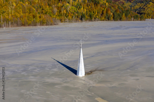 Abstract aerial view of church tower with cross and shadow, flooded by copper mining residuals and mud