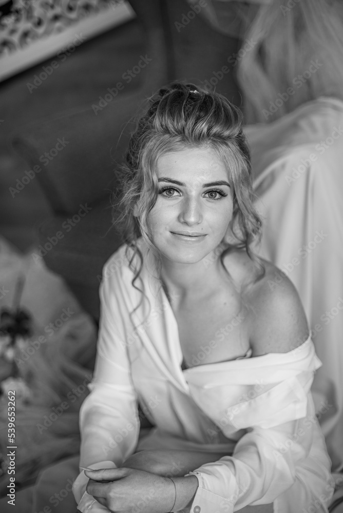 Young beautiful bride with wedding hairdo and makeup in the morning wearing a white silk negligee in the bedroom. wedding morning Young beautiful bride with wedding hairdo and makeup in the morning wearing a white silk negligee in the bedroom. wedding morning