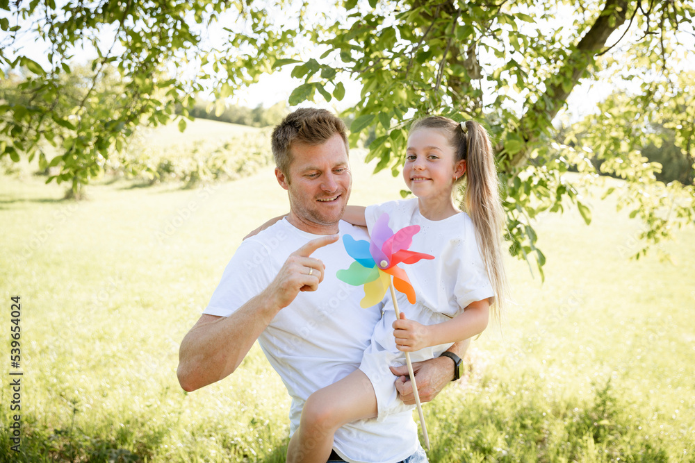Fototapeta premium Father and daughter cuddle and have fun outside in nature with colorful pinwheel and are happy