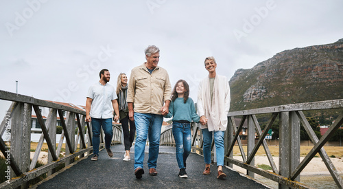 Family, walking and travel with a girl and grandparents holding hands on a pier while on holiday or vacation together. Love, trust and children with a man, woman and granddaughter boding on a walk