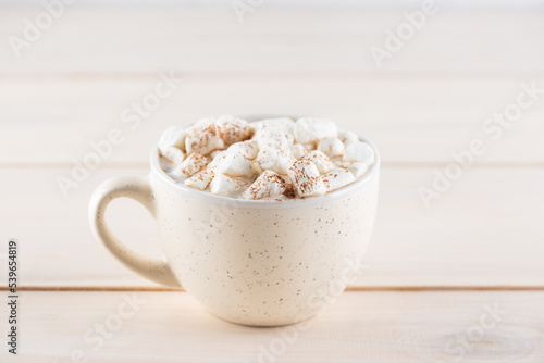 Hot cocoa with marshmallows in a white mug on a wooden table.