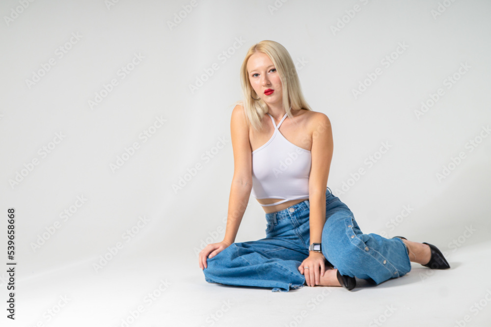 Young attractive blonde girl in a top and jeans posing on a white background
