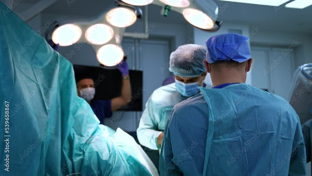 Surgeons team finishing the operation conducted in collaboration. Male assistant adjusting the lamp for brighter vision of doctors. Surgeons team finishing the operation conducted in collaboration. Male assistant adjusting the lamp for brighter vision of doctors.