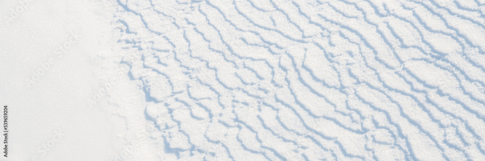 Beautiful winter background with snowy ground. Natural snow texture. Wind sculpted patterns on snow surface. Wide panoramic texture for background and design. Beautiful winter background with snowy ground. Natural snow texture. Wind sculpted patterns on snow surface. Wide panoramic texture for background and design.