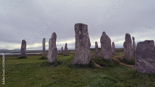 Moving around the standing stones or megaliths of the Callanish or Calanais stone circle in a cloudy evening. Sun peeking through the could, magic, ancient, neolithic atmosphere. Archaeological sites. photo