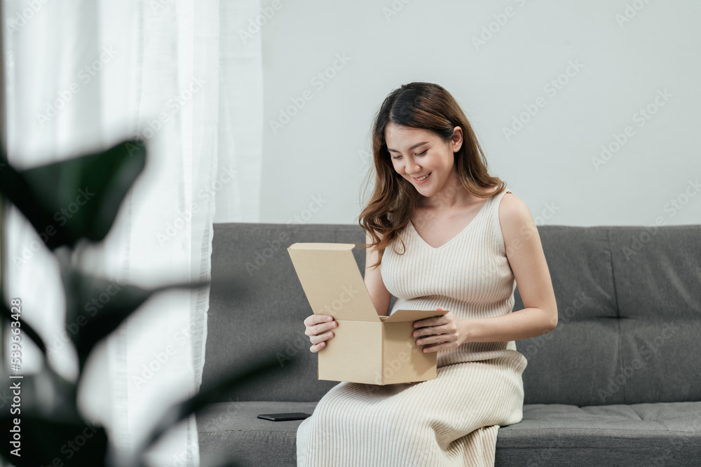 Beautiful pregnant Asian woman happy sitting on the sofa and opening parcel box receive from online shopping in the living room. Pregnancy happy relaxation at home. Beautiful pregnant Asian woman happy sitting on the sofa and opening parcel box receive from online shopping in the living room. Pregnancy happy relaxation at home.