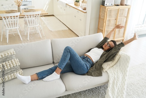 Young african american girl stretching after day sleep, resting, lying on comfortable couch at home