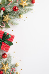 Christmas concept. Top view vertical photo of giftbox with bow pine branches in snow decorated with red baubles gold star ornaments candy canes and confetti on isolated white background with copyspace