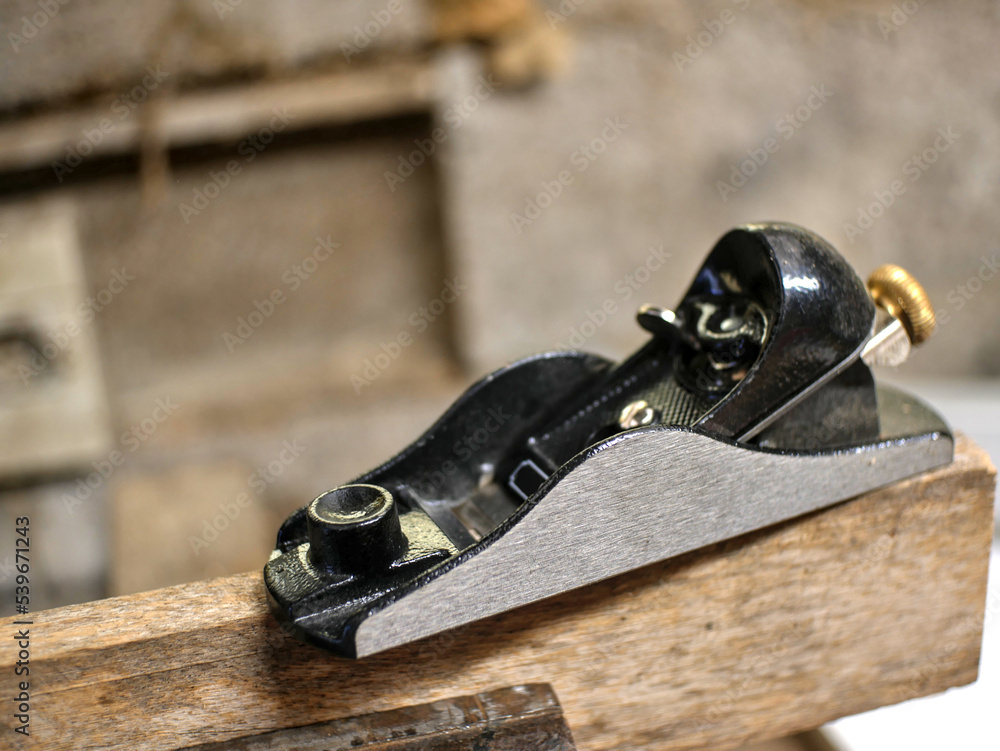 Partially blurred small plane, placed on a board, held by a vice, in a carpentry workshop Partially blurred small plane, placed on a board, held by a vice, in a carpentry workshop