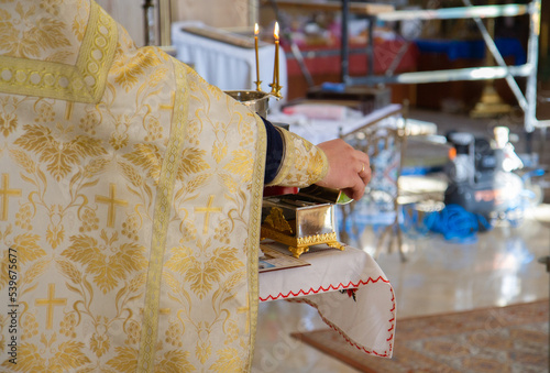 a metal bowl for baptism and three lighted candles, the priest's hands near the bowl