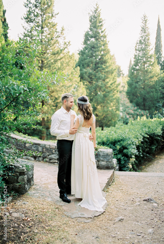 Groom hugs bride on a paved path in the park among the trees