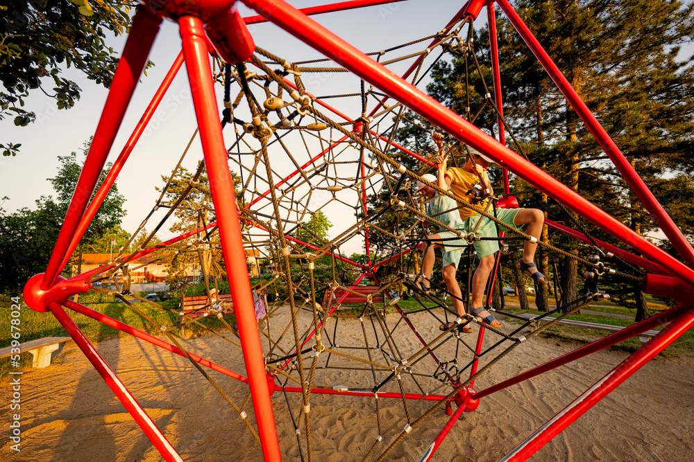 Brothers play in rope polyhedron climb at playground outdoor.
