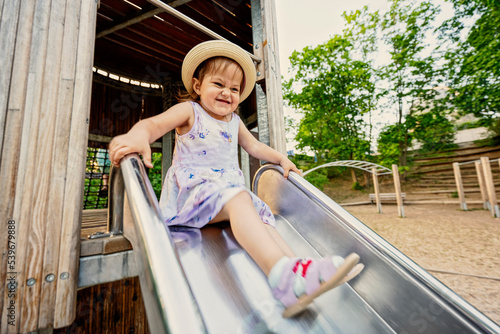 Baby girl slides in children's playground toy set in public park.