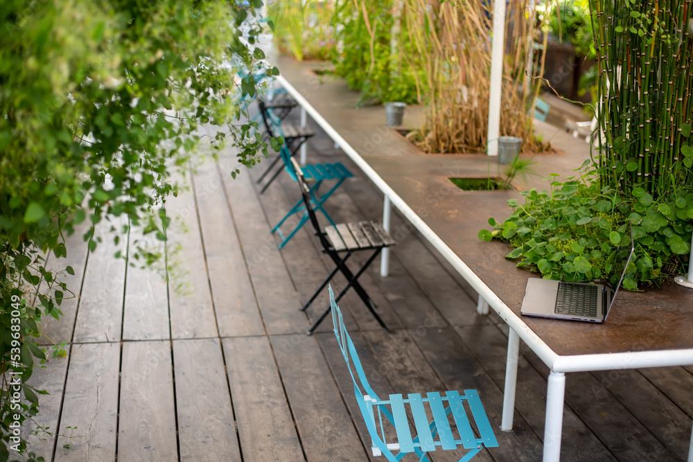Green open space for coworking, freelancer, relaxation, coffee, food. Free place to work in nature. Remote nomad digital laptop on the table. Outdoor table with laptop. Concept of sustainability
