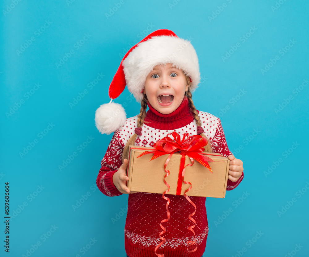 Amazed excited little girl in santa hat holding Christmas present Amazed excited little girl in santa hat holding Christmas present