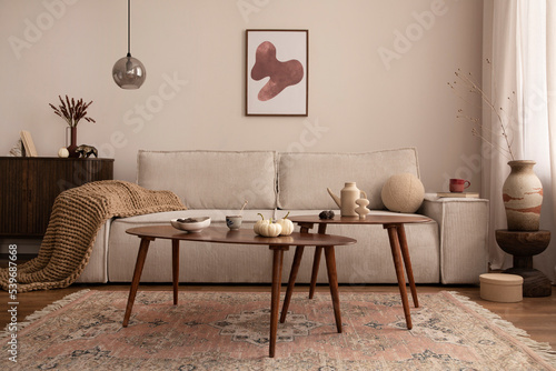 Domestic and cozy interior of living room with mock up poster frame, corduroy sofa, wooden coffee table, round pillows, plaid, vintage rug, wooden floor, lamp and personal accessories. Home decor.