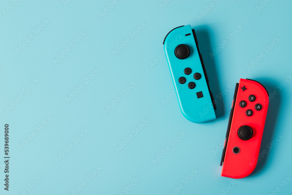 Foto Stock Milan, Italy-Oct. 2022: Nintendo Switch Game Console game  controller in different colors, neon blue and red isolated on blue  background copy space. | Adobe Stock