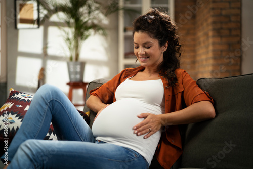  Pregnant woman sitting on a sofa and caressing her belly