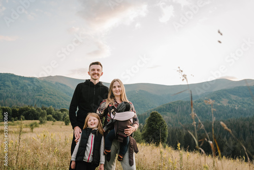 Family with kids hiking in mountains. Young tourists on top of a mountain enjoying valley view sunset. Happy mom, and dad with a backpack son and daughter. Holiday trip concept. World Tourism Day.